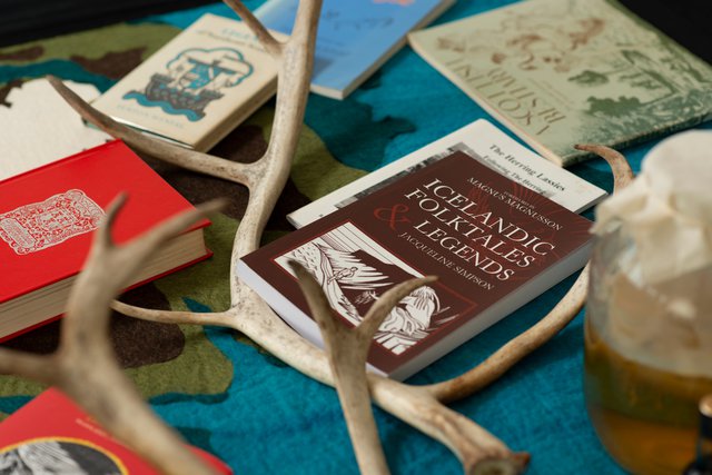 Deatil photograph showing various books jumbled with reindeer antlers and a glass fermenting jar lying on a felt rug.